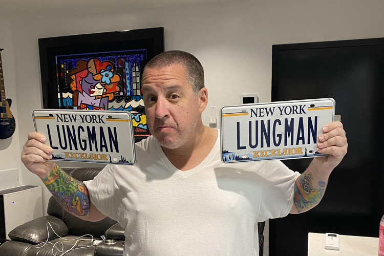 dr. noah greenspan holding his "lungman" ny license plates in his nyc offices of his pulmonary wellness foundation