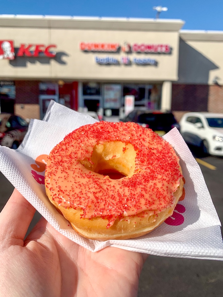 the dunkin' spicy ghost pepper donut with pink icing and spinkles outside of a dunkin' donuts